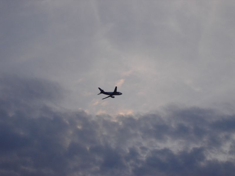 a commercial airplane flying against a cloudy sky