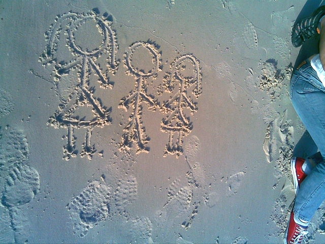 two people sitting on the sand writing letters