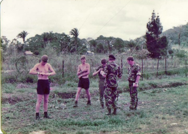 a group of soldiers stand in a grassy field with one soldier using the same tool