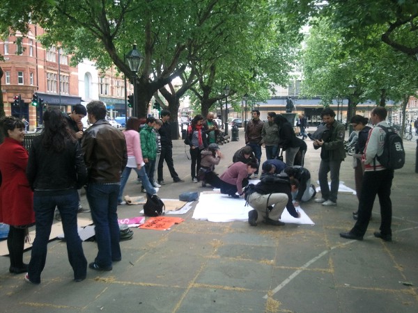 people standing and sitting around a person laying on a paper on a street