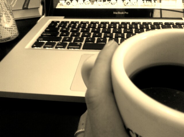 a person holding a cup of coffee over a laptop