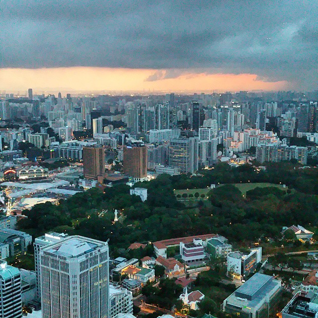 an aerial view of tall buildings near trees and cloudy sky
