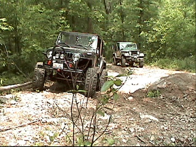 two off road vehicles drive up a wooded trail
