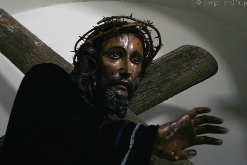 statue of jesus carrying a cross with a wooden stick