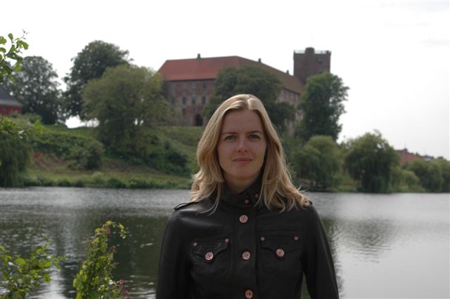 a lady standing near a lake with a house in the background