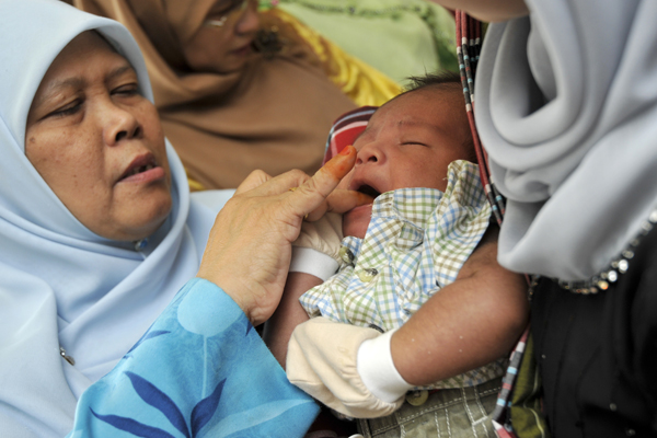 a woman holds a baby and is wearing a headscarf