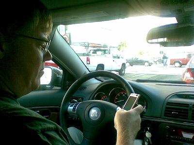 a man is in his car while driving and has a cell phone in his hand