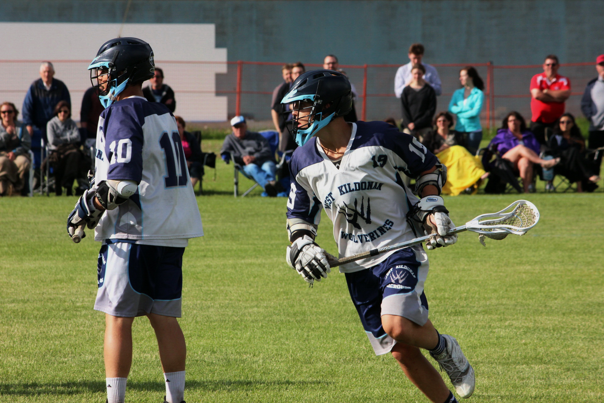 two boys are playing lacrosse on the field with people in the background