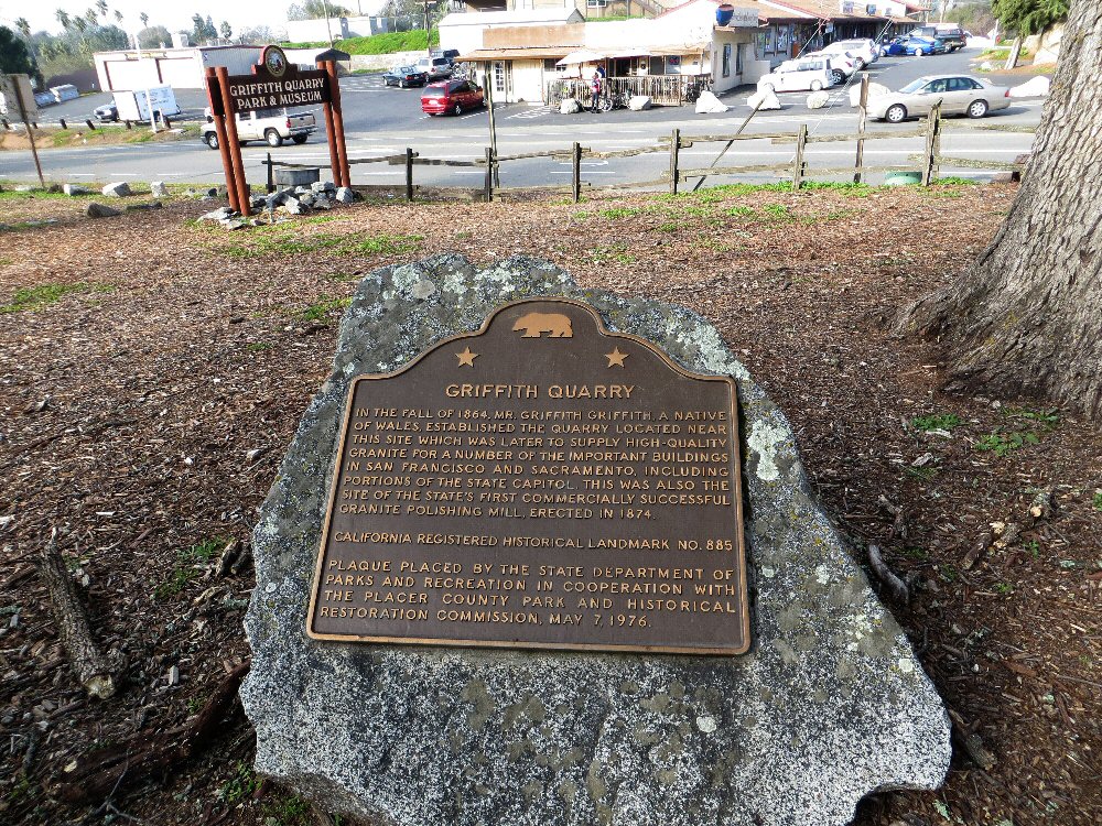 a stone marker that reads a town square, located on a grassy lawn with trees and cars