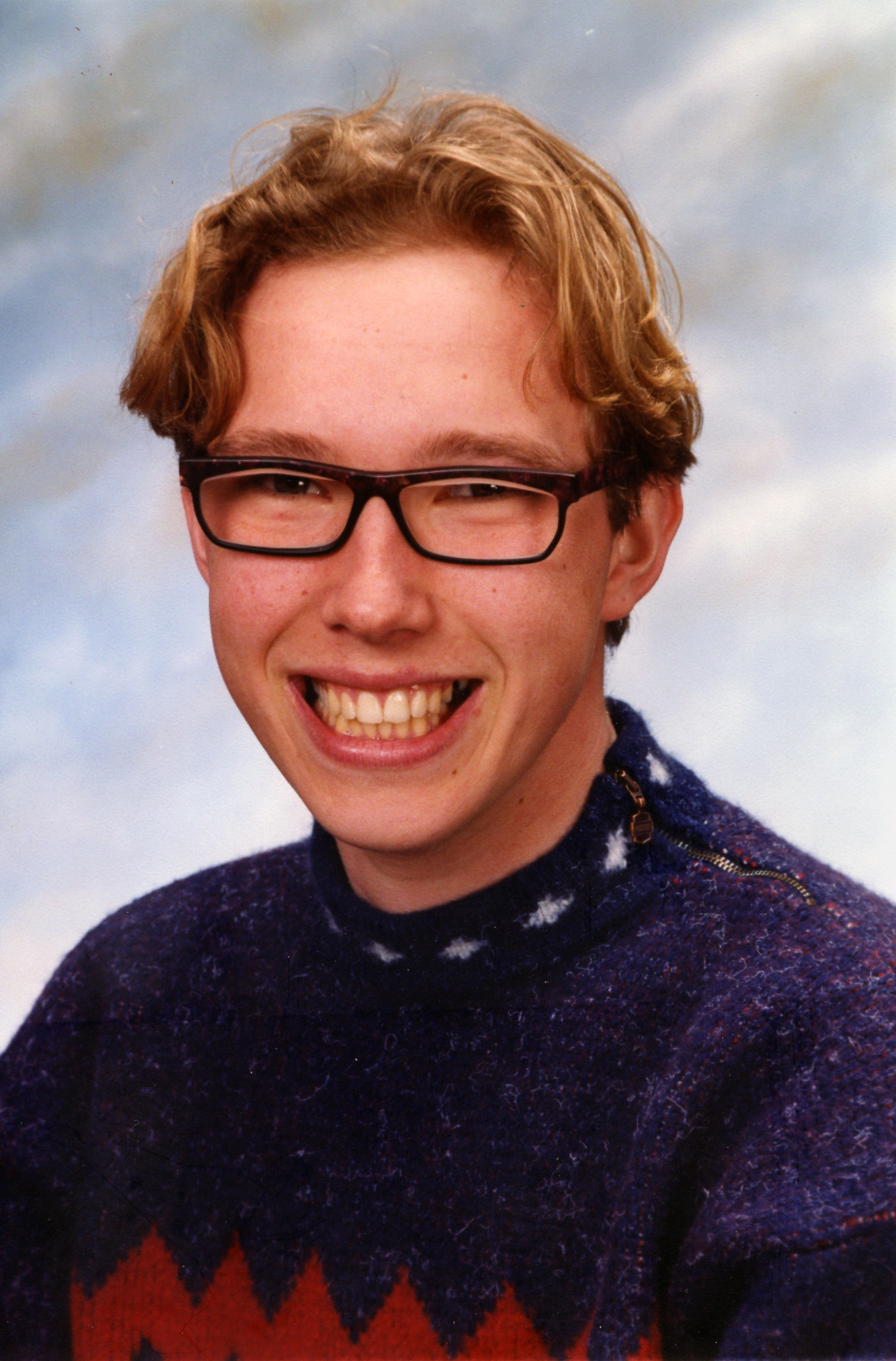 a smiling man is wearing glasses and a sweater