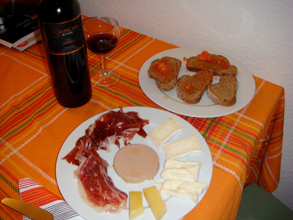 the cheese and meats are on plates next to the wine