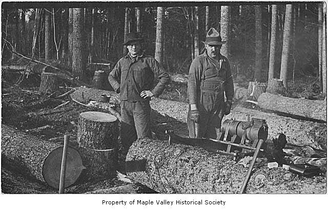 two men in the woods are standing beside some logs
