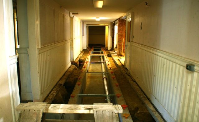 a long hallway with water pipes and a toilet