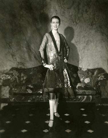 a woman in a long shiny skirt stands on a black and white checkered carpet