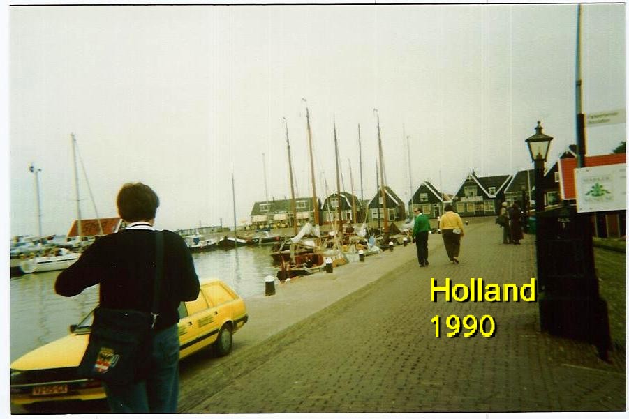 people walking down an old cobble stone road towards sailboats in holland, 1990s