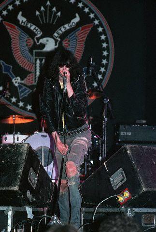 man in leather jacket and jean shorts on stage singing
