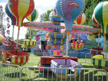 carnival rides in grassy area with people riding them