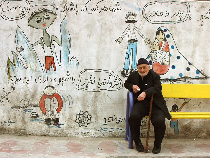 a man sitting on a yellow bench in front of a wall with arabic art