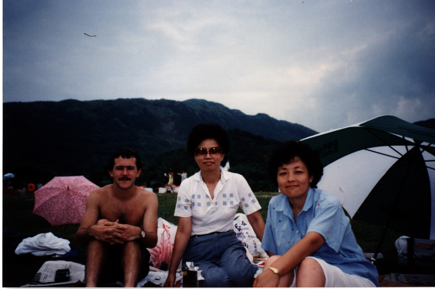 two women and a man sitting at a picnic near a mountain