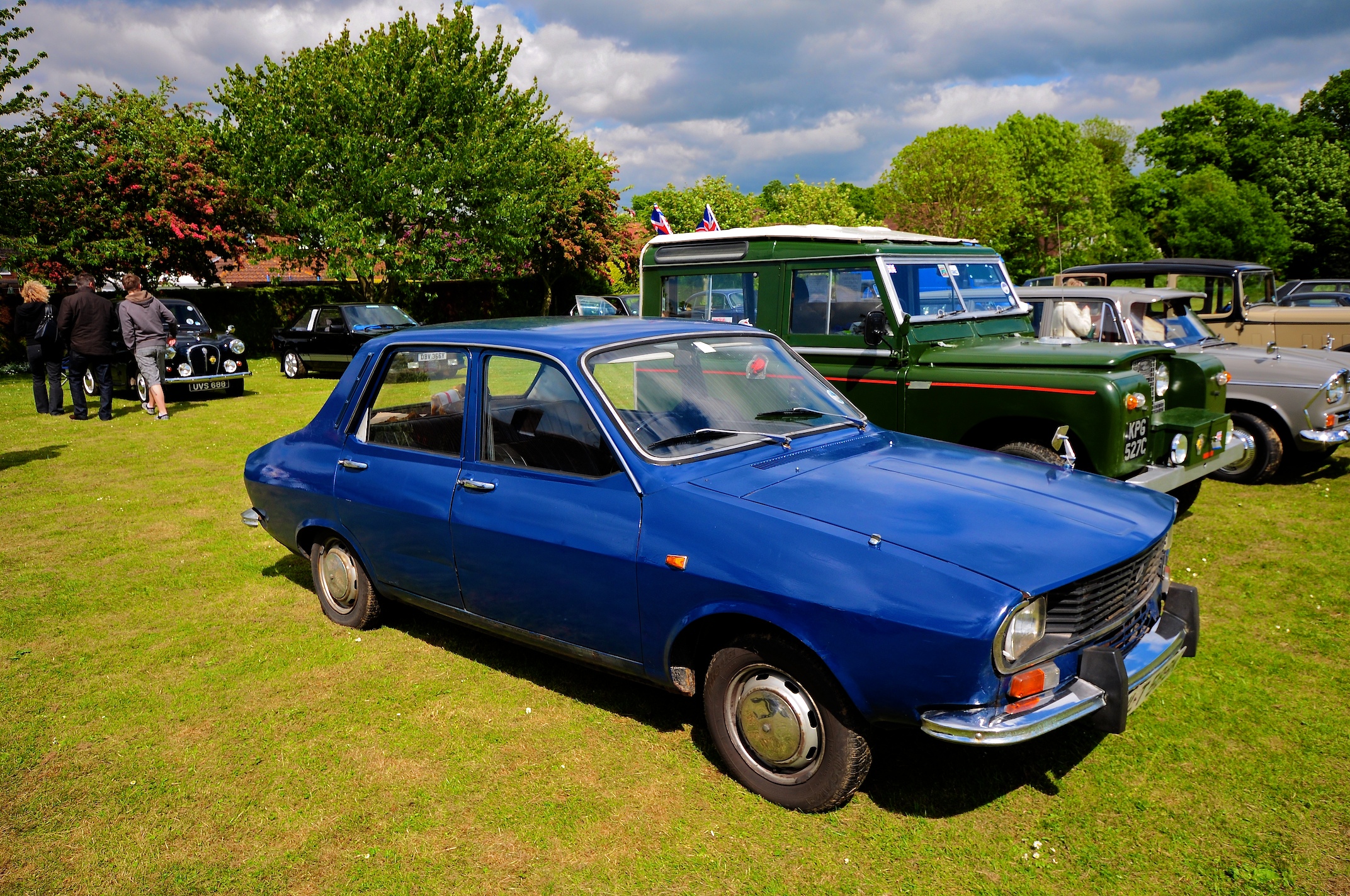 an older blue car is in the middle of a group of other cars