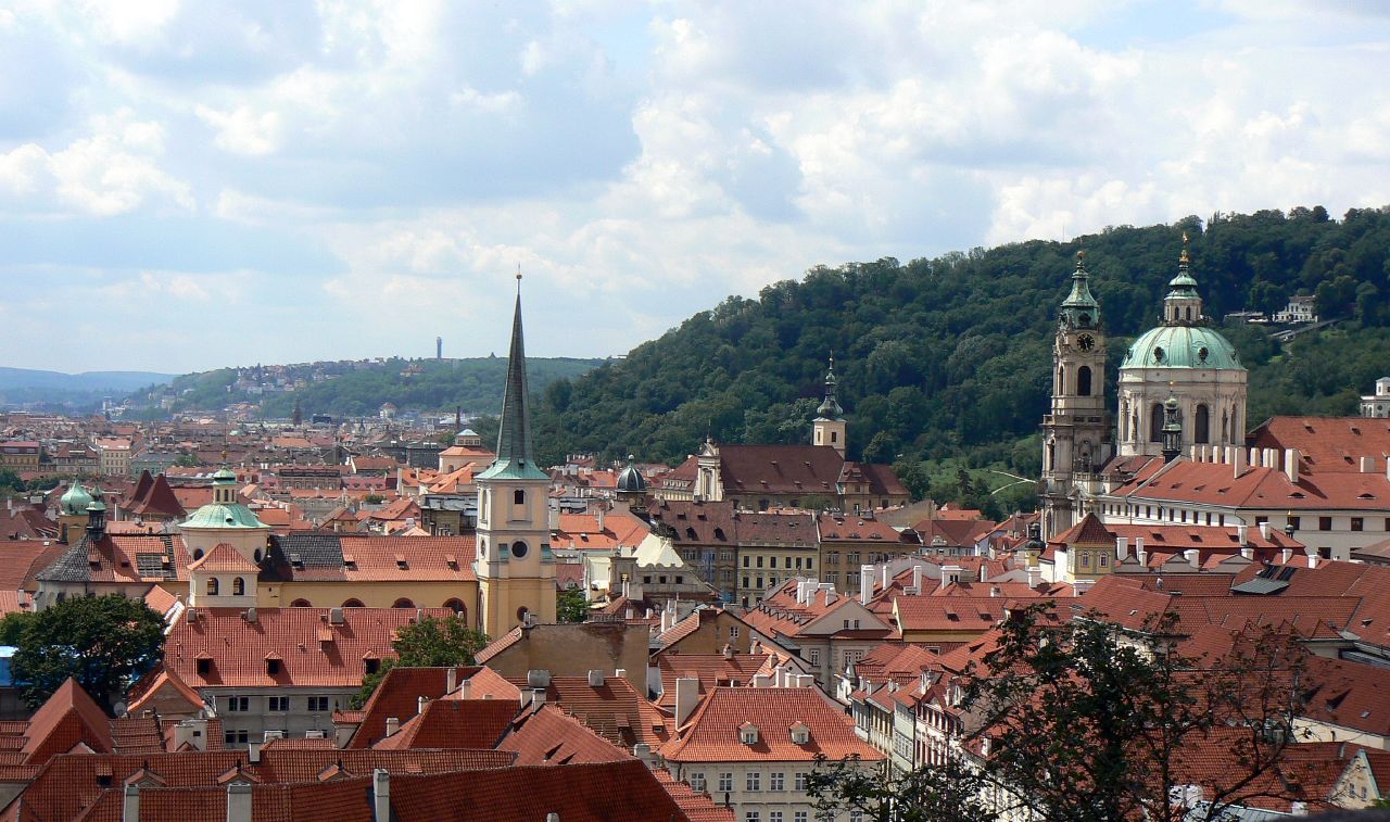 a city with many red roofs, trees, and hills