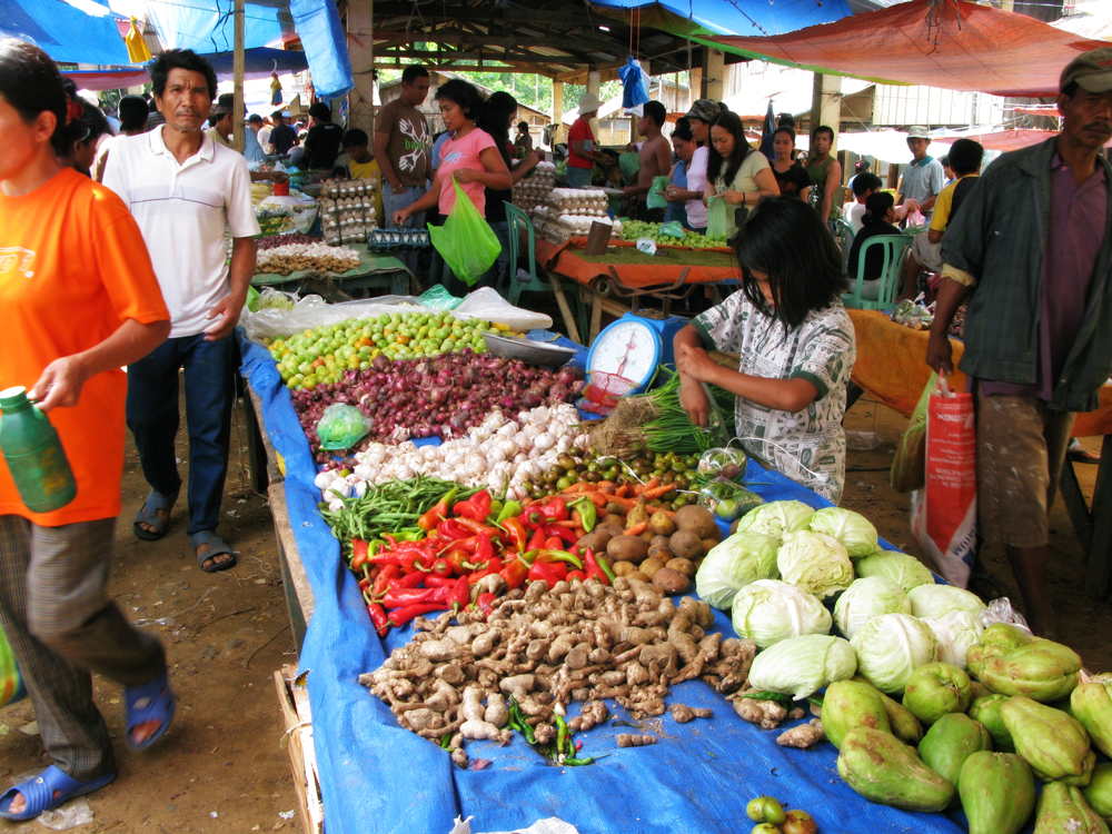 people shopping at an open market with lots of vegetables