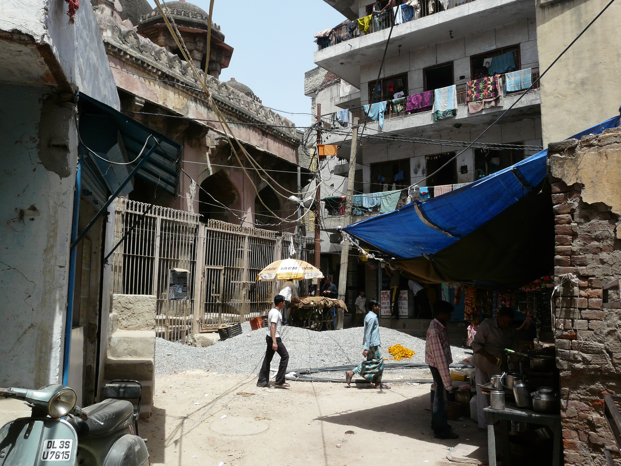 a small dirt street in front of a building with people standing and hanging out on it