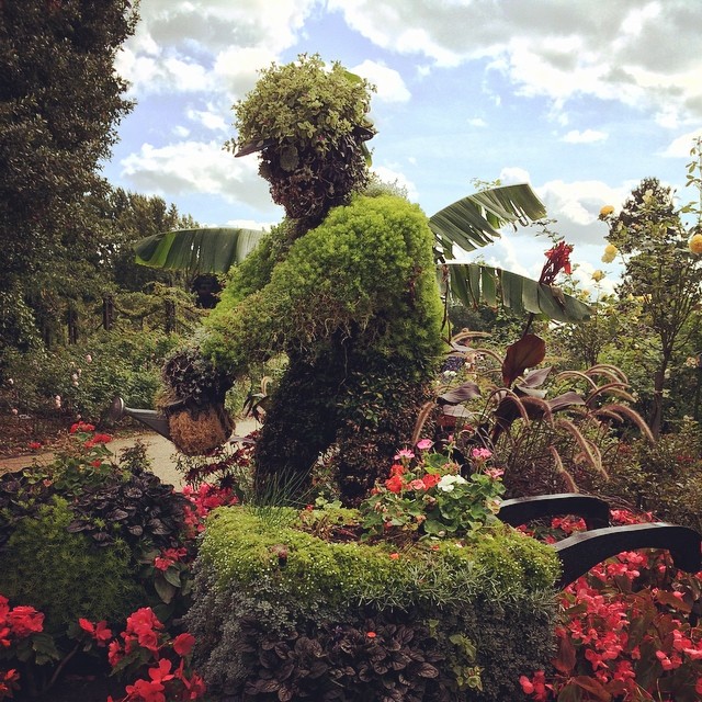 a green statue in a garden surrounded by flowers