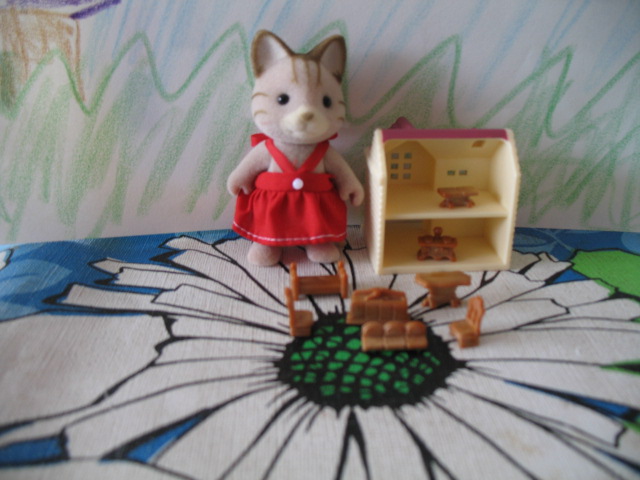 a little girl in a red dress is next to a cat doll and a wooden truck