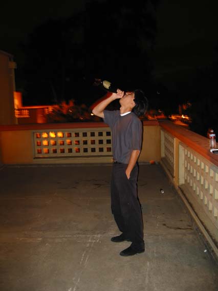 a young man drinking from a bottle while standing on a balcony at night