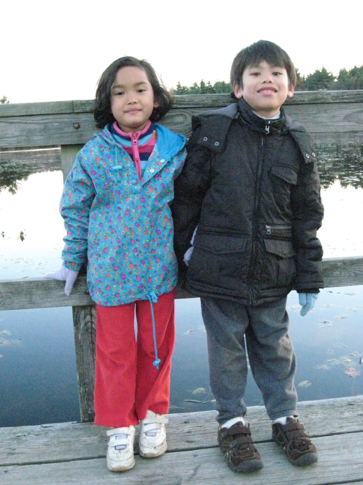 two children standing next to each other next to a fence