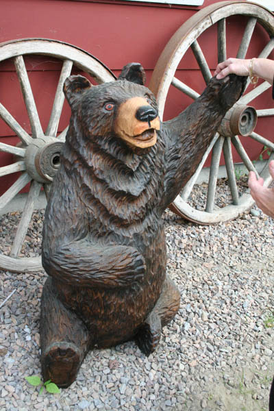 there is a teddy bear statue being posed next to two antique white wagon wheels