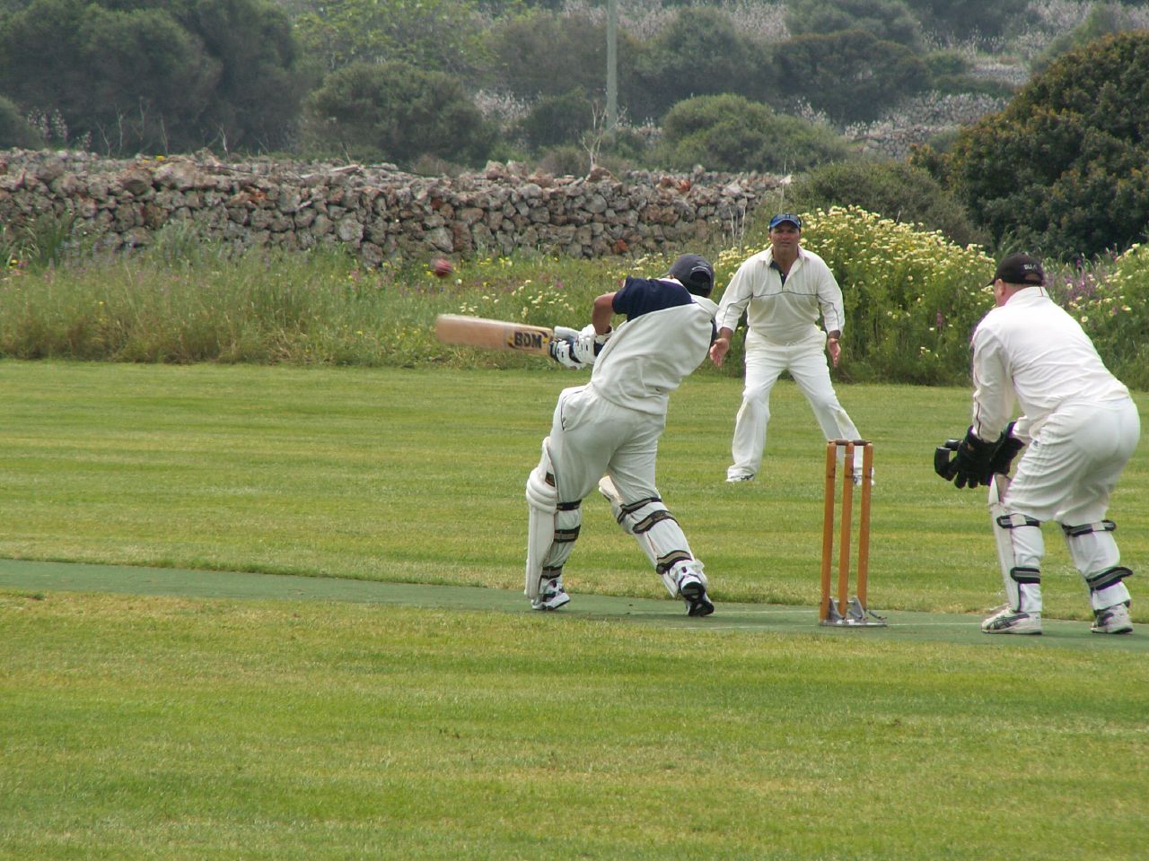 three men in white suits playing cricket on grass