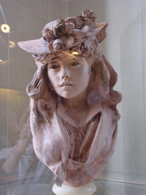 a glass display case of a sculpture with a woman wearing a hat