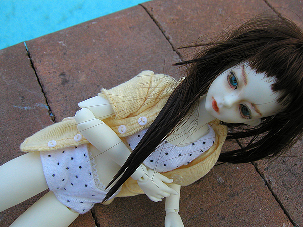 a doll with long hair laying next to a blue pool