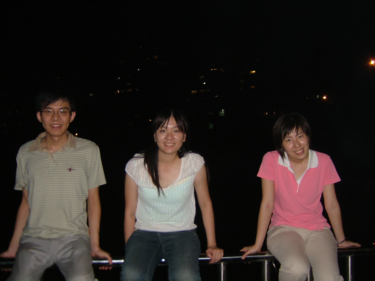three people posing on a railing by a body of water