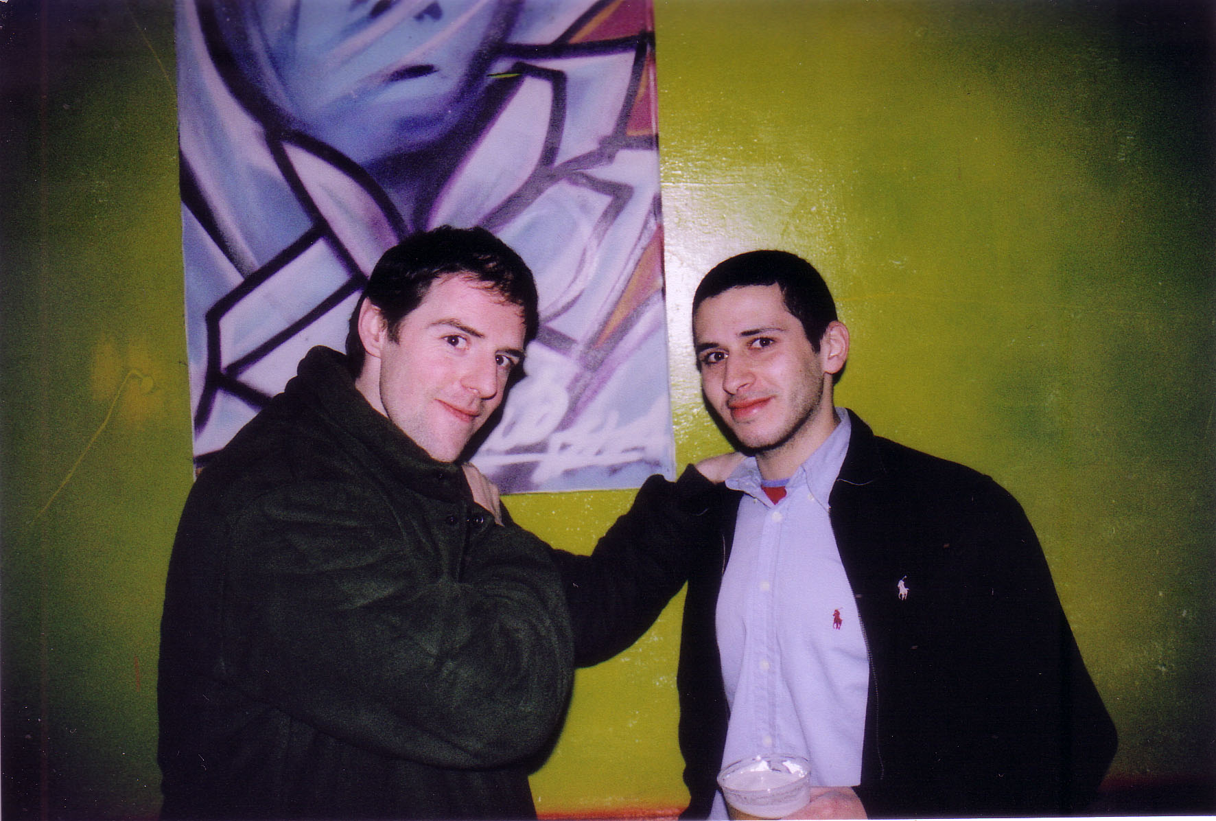 two men posing in front of a painting in front of the same wall