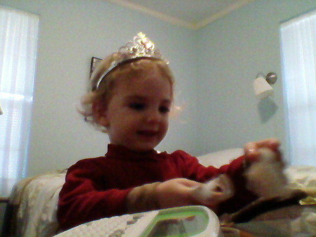 a toddler holds a teddy bear while wearing a princess crown