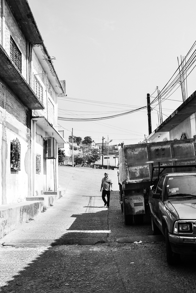 black and white po of a woman walking through street next to vehicles
