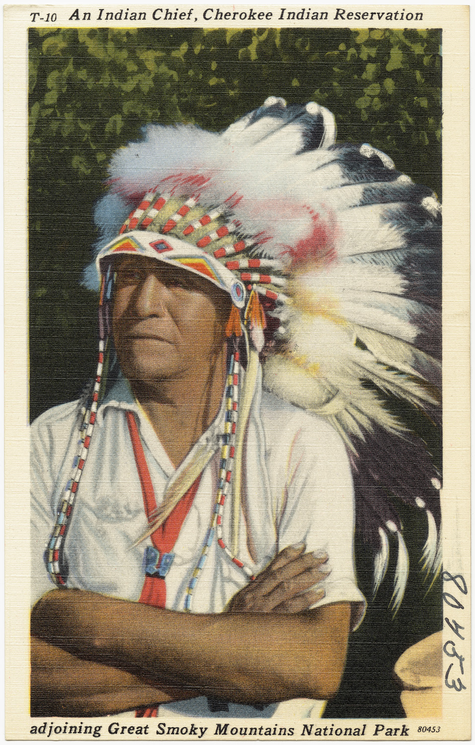 a man wearing an indian headdress sitting down with his arms crossed