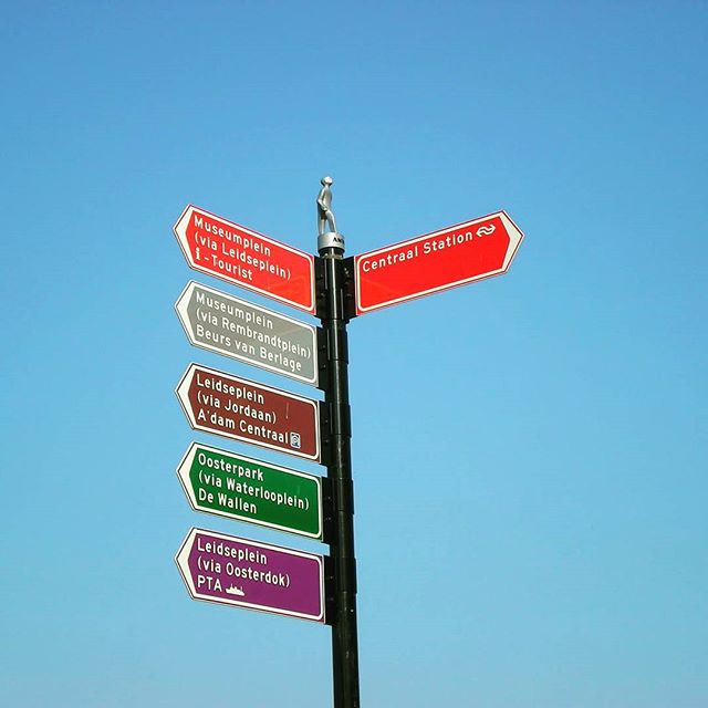 a pole with signs indicating different directions on a clear blue sky
