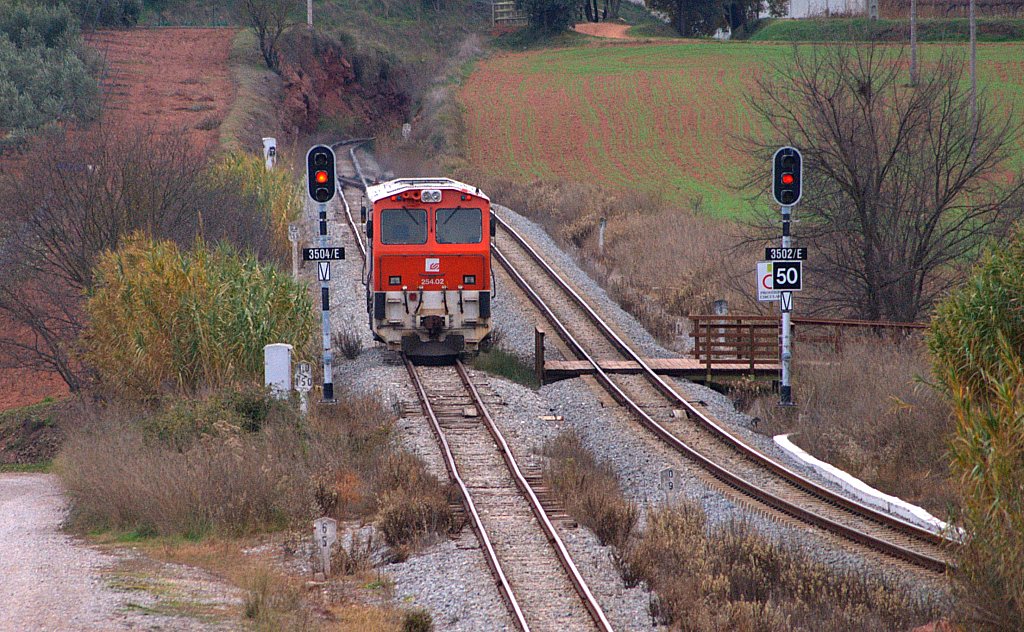 a red train is riding the tracks in a rural area