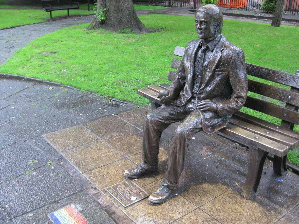 a bronze statue of a man sitting on top of a wooden bench