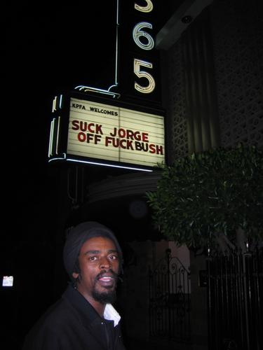 a black man stands in front of the side of a marquee sign
