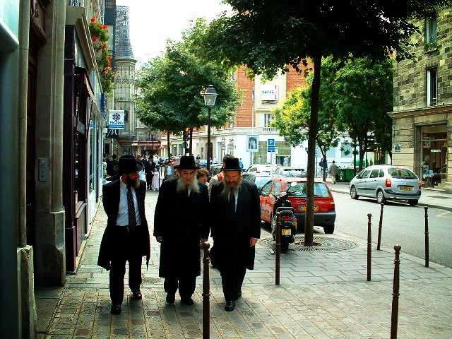 three jewish men walking on the sidewalk of a busy city