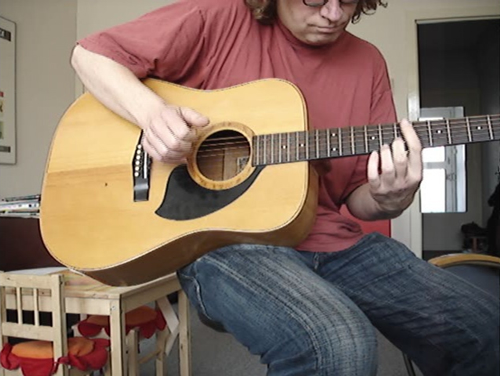 a man sitting with an acoustic guitar
