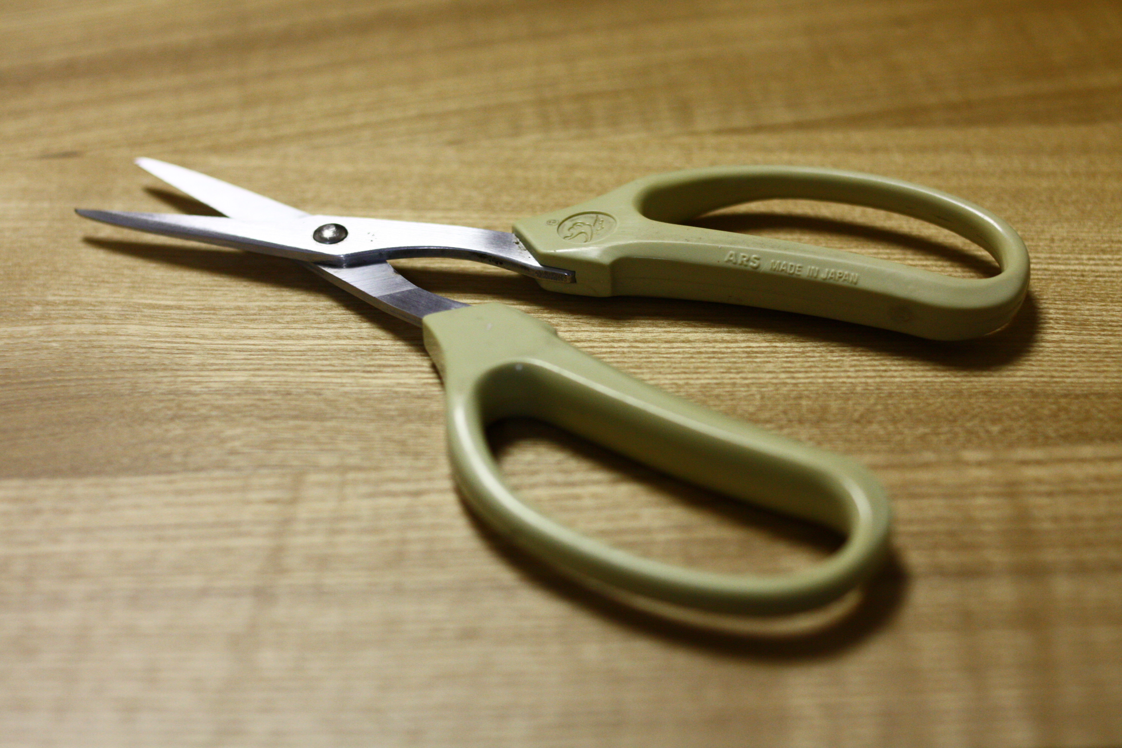 the pair of scissors is on the wooden table