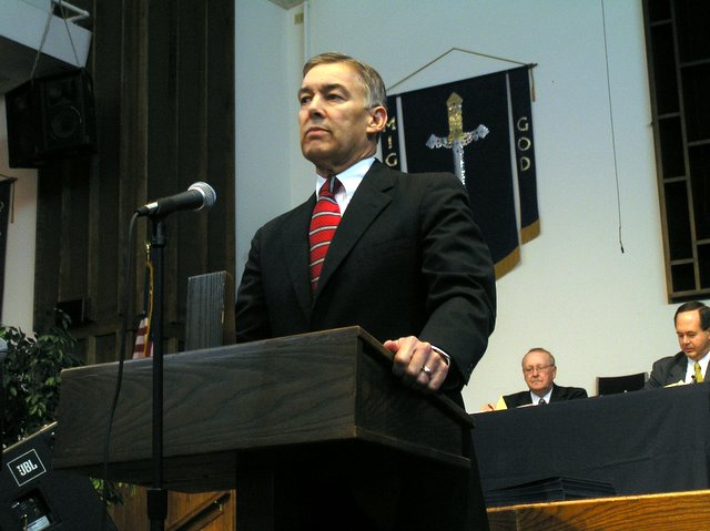 a man is standing behind a microphone in front of a room full of people