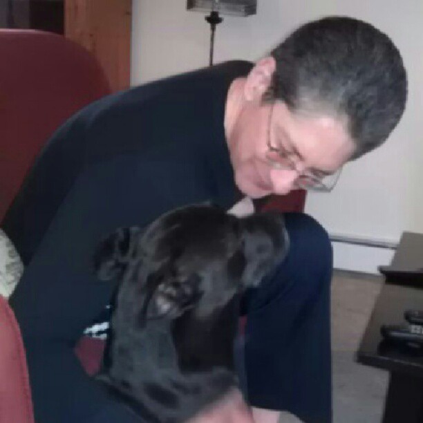 a man hugging a black dog in a living room