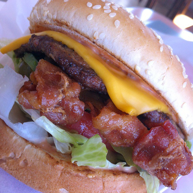 a bacon cheeseburger on a bun with lettuce and tomato